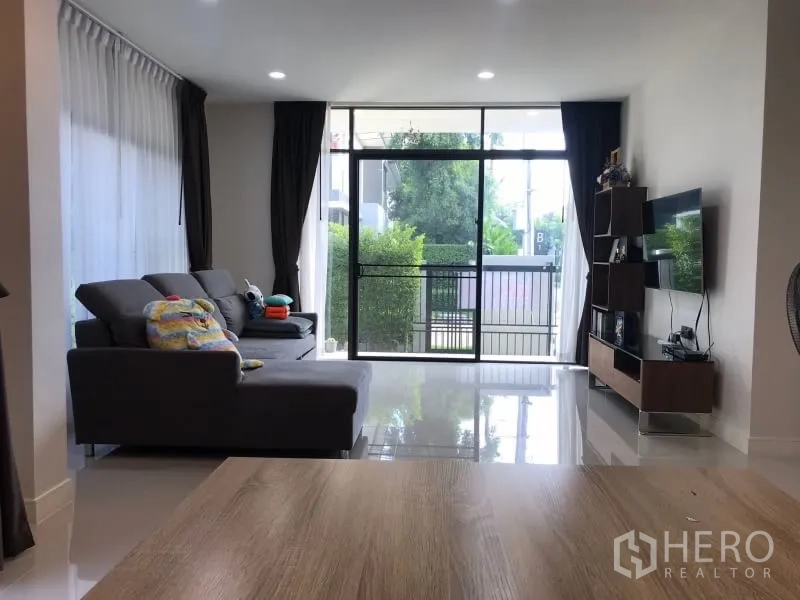 Detached House for rent in Bang Kapi, Bangkok - Bright living room with floor-to-ceiling sliding doors, gray sofa and TV unit.
