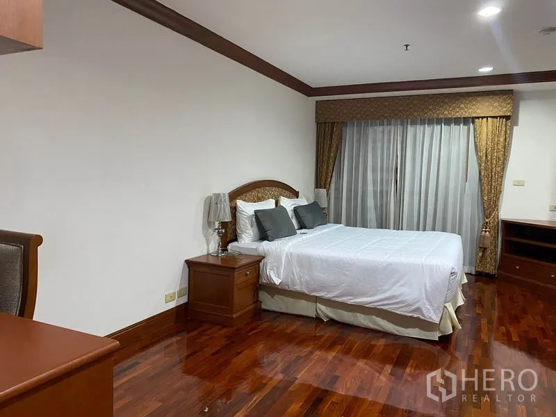 Condominium for rent in Watthana, Bangkok - Third bedroom with bed, bedside table and sliding glass doors hidden by curtains.
