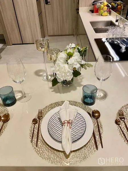 คอนโด ให้เช่าในWatthana, Bangkok - การจัดโต๊ะทานอาหารบนไอส์แลนด์ครัวพร้อมจาน แก้วไวน์ และแจกันดอกไม้