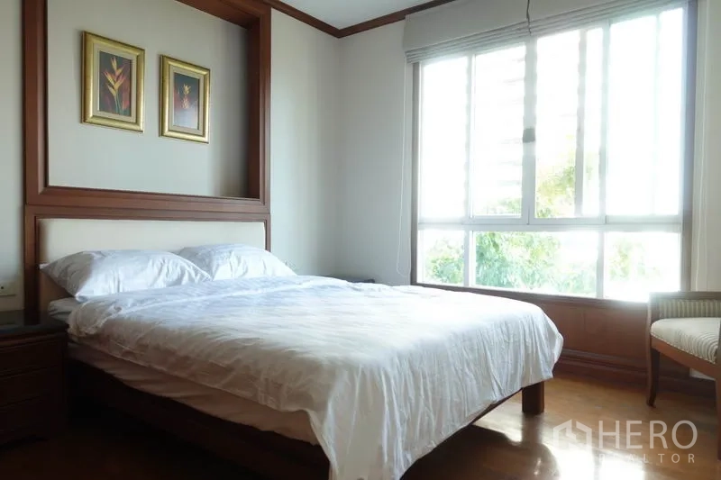 Condominium for rent in Khlong Toei, Bangkok - Sunlit bedroom with large window and minimalist wooden furniture.