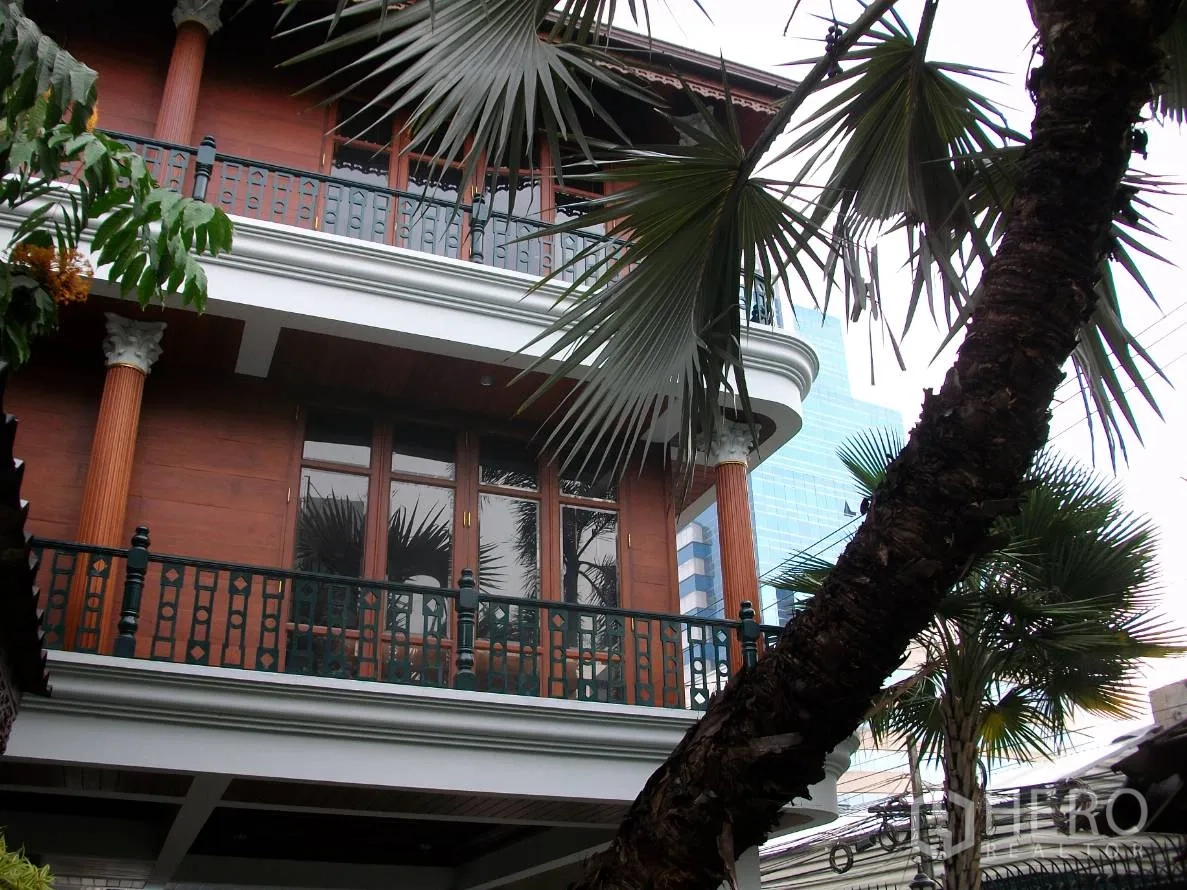 บ้าน ให้เช่าในKhlong Toei, Bangkok - ด้านหน้าบ้านสไตล์ไทยสูงสองชั้น มีระเบียง เสา และต้นปาล์มสูง.