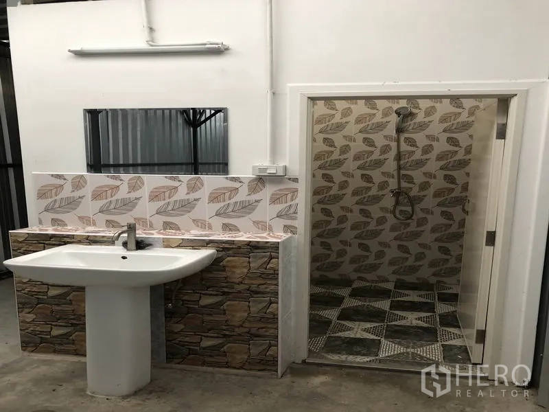 Warehouse for rent in Pak Kret, Nonthaburi - On-site restroom and shower area with patterned tiles and pedestal sink inside the facility.