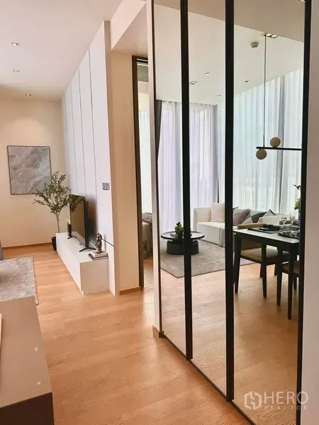 Condominium for rent in Pathum Wan, Bangkok - Hallway view to an open-plan lounge and dining space with tall curtains and a minimalist TV console.
