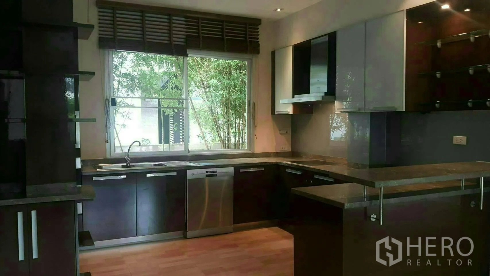 Detached House for rent or sale in Prawet, Bangkok - Modern U-shaped kitchen with large window, dark cabinetry and stainless-steel appliances.