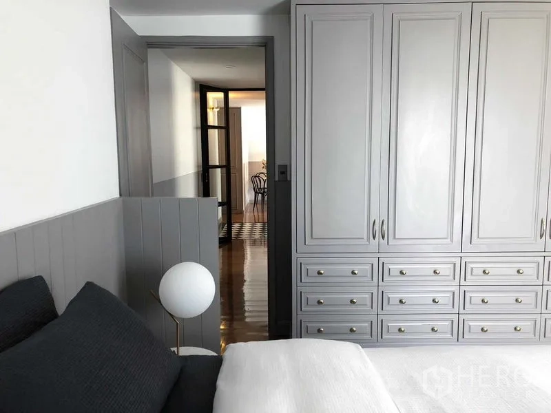 Condominium for sale in Watthana, Bangkok - Bedroom with built-in gray wardrobes, bedside lamp and a view to the hallway through a glass door.