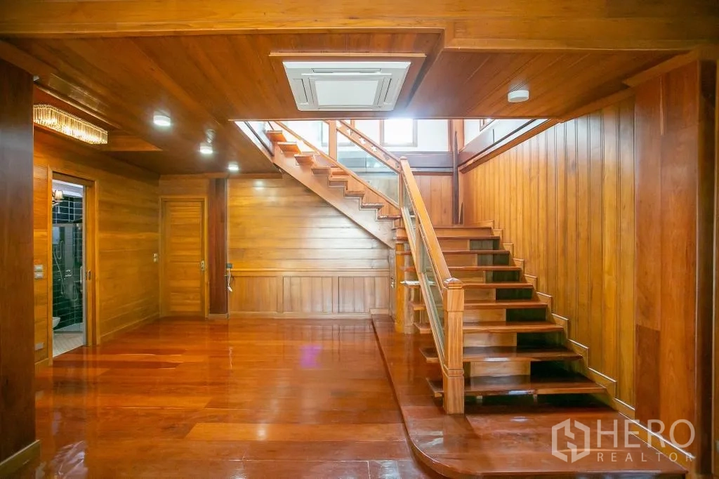 Detached House for rent or sale in Huai Khwang, Bangkok - Spacious wood‑clad living hall with staircase, recessed lighting and bathroom access.