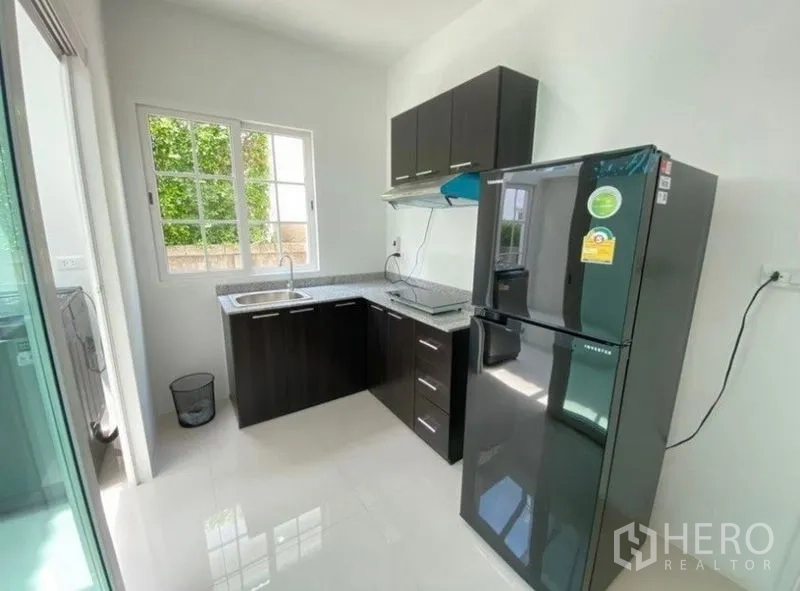 Detached House for rent or sale - L-shaped kitchen with dark cabinets, stone countertop, window and a large refrigerator.