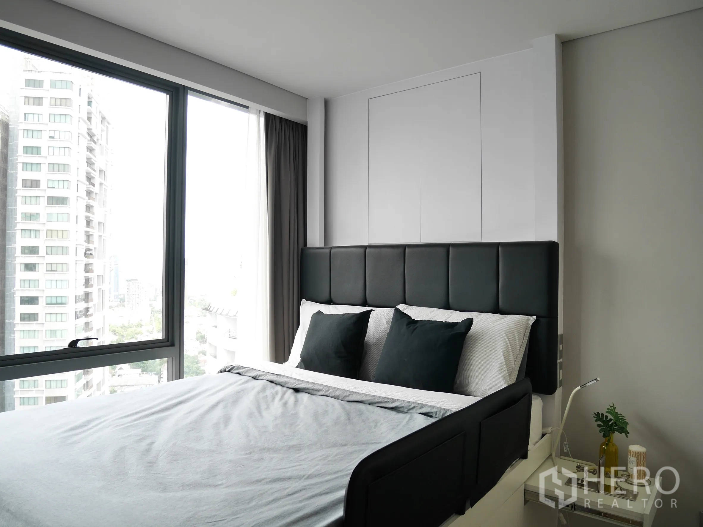 Condominium for rent in Khlong Toei, Bangkok - Sunlit bedroom with large window, upholstered headboard, bedside table, and city views.