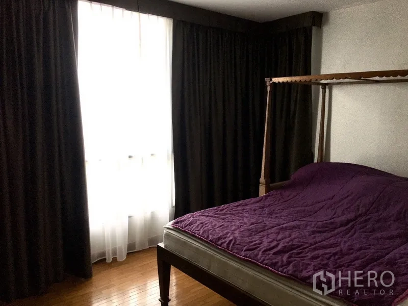 Condominium for rent in Pathum Wan, Bangkok - Cozy bedroom with a four-poster bed, dark curtains, and a large window.