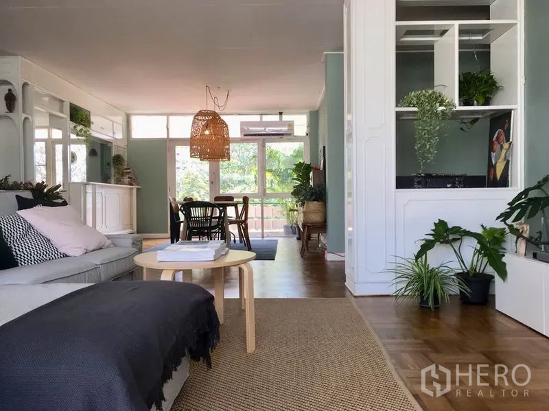 Apartment for rent in Khlong Toei, Bangkok - Open-plan lounge and dining area with rattan pendant lights, wood floors, and full-height glass doors to the balcony.