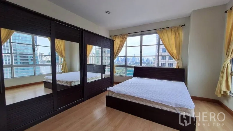 Condominium for rent in Khlong Toei, Bangkok - Primary bedroom with expansive windows, city views, dark wood bed, and mirrored wardrobes.