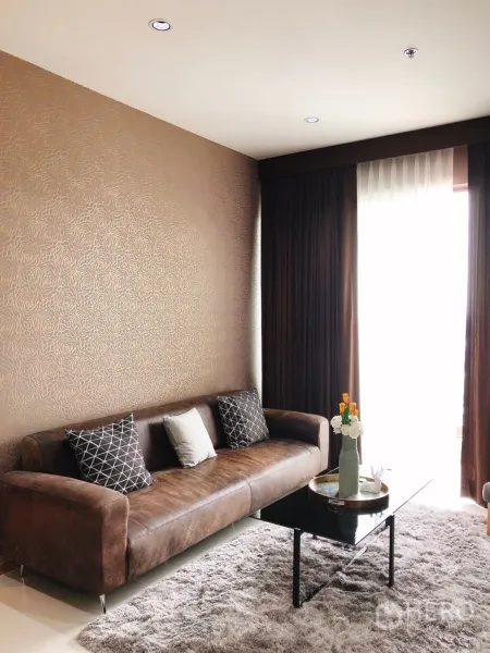 คอนโด ให้เช่าในKhlong Toei, Bangkok - มุมห้องนั่งเล่นพร้อมโซฟาสีน้ำตาล หมอนลาย และโต๊ะกลางกระจก