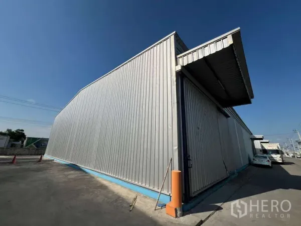 Warehouse for rent in Lat Krabang, Bangkok - Exterior of corrugated metal warehouse with loading canopy and wide driveway under clear blue sky in Lat Krabang, Bangkok.