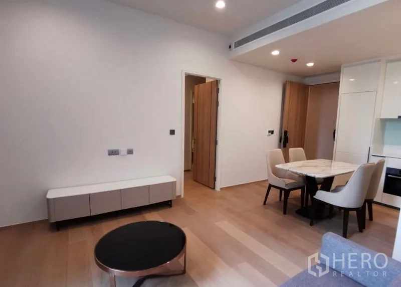 公寓 出租在Bang Rak, Bangkok - 客餐厅一体视角，圆形茶几、电视柜与用餐区相连，木地板清新。