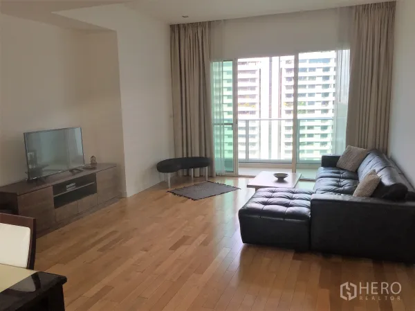 คอนโด ให้เช่าในKhlong Toei, Bangkok - ห้องนั่งเล่นสว่าง โซฟาหนังสีดำ พื้นไม้ และประตูกระจกเปิดสู่ระเบียงชมวิวเมือง