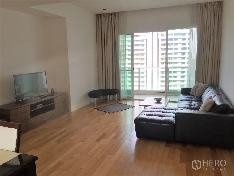 คอนโด ให้เช่าในKhlong Toei, Bangkok - ห้องนั่งเล่นสว่าง โซฟาหนังสีดำ พื้นไม้ และประตูกระจกเปิดสู่ระเบียงชมวิวเมือง