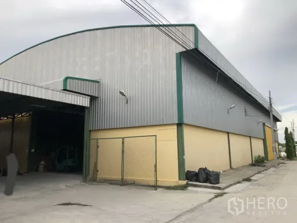 Warehouse for rent in Lat Krabang, Bangkok - Front exterior of warehouse with green-trim metal cladding, fenced side entry, and concrete driveway.