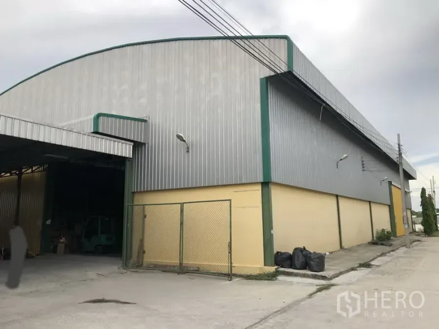 Warehouse for rent in Lat Krabang, Bangkok - Front exterior of warehouse with green-trim metal cladding, fenced side entry, and concrete driveway.