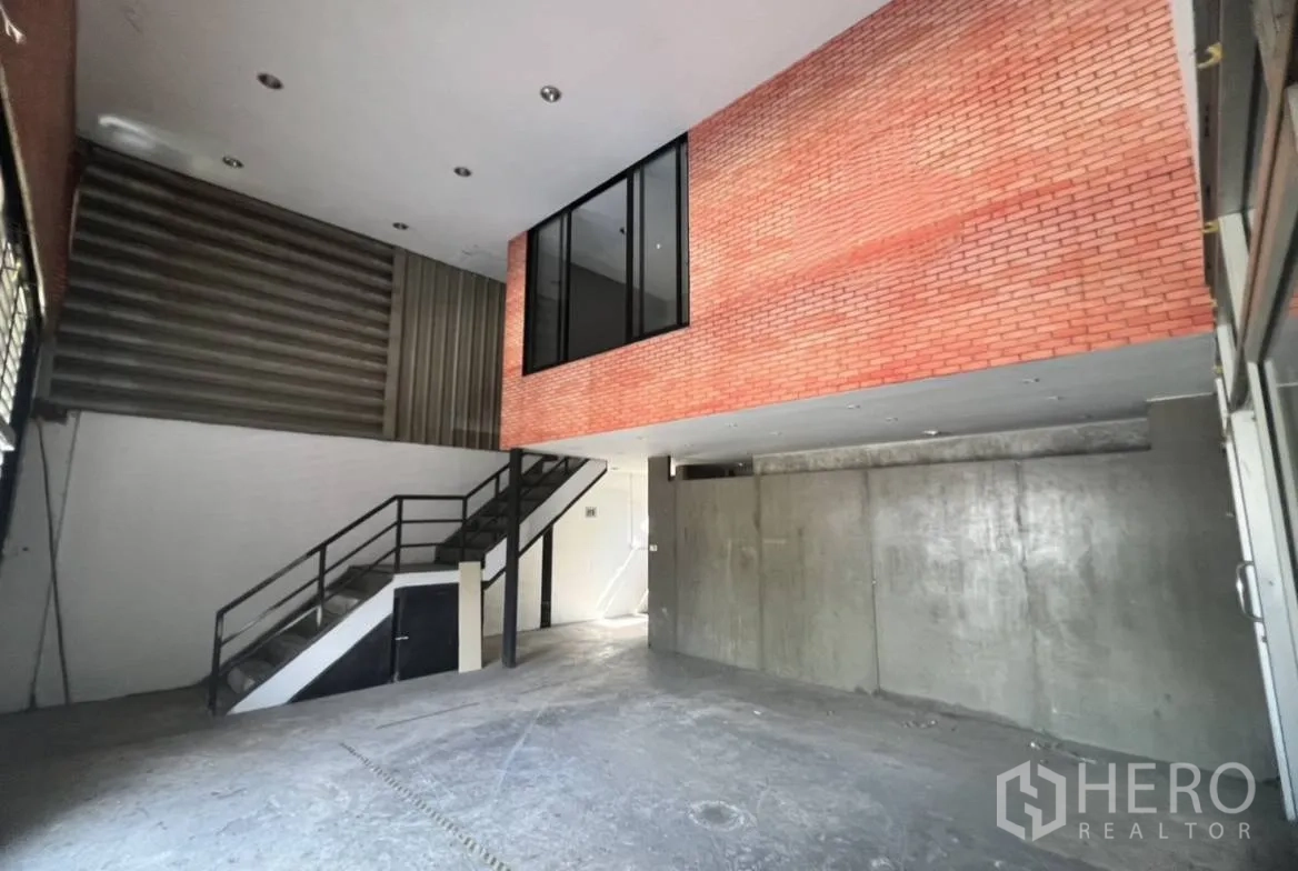 Warehouse for rent in Suan Luang, Bangkok - Entrance hall with high ceiling, brick mezzanine office, and a metal staircase.