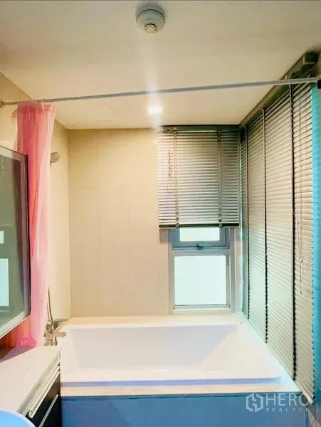 Condominium for rent - Bathroom with soaking bathtub beside windows with blinds and a shower rail.