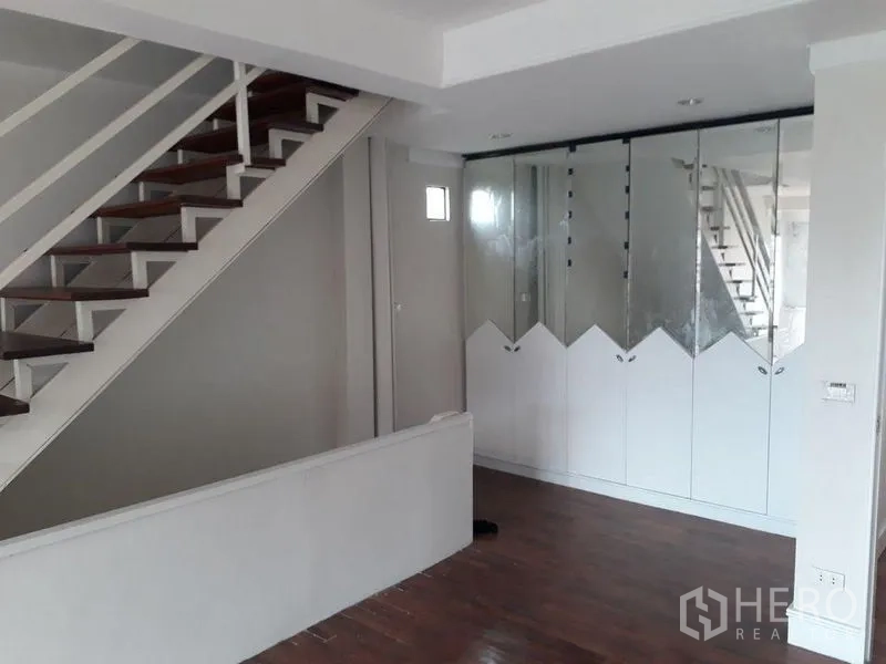 Townhouse for sale in Bang Kapi, Bangkok - Stair hall with wooden steps and built-in mirrored wardrobes beside a white wall.