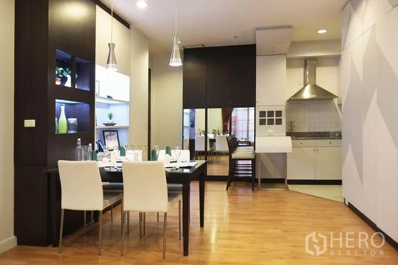 Condominium for rent in Khlong Toei, Bangkok - Dining area with pendant lights beside an open kitchen and mirrored wall.