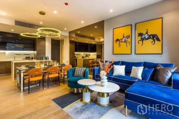 Condominium for rent in Pathum Wan, Bangkok - Open‑plan lounge and dining with blue sofa, bold artwork and modern lighting.