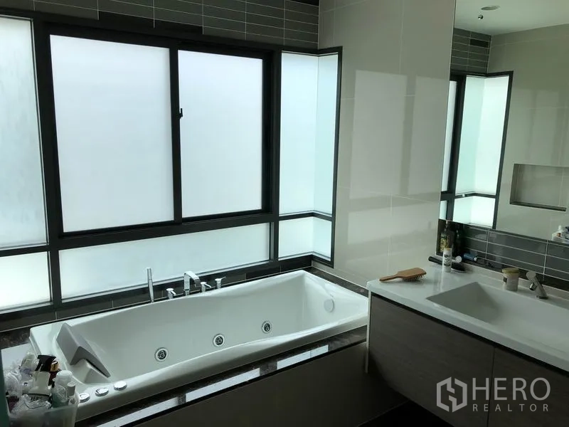 Detached House for rent or sale in Bang Kapi, Bangkok - Bathroom featuring a large built-in bathtub, frosted windows and long vanity.