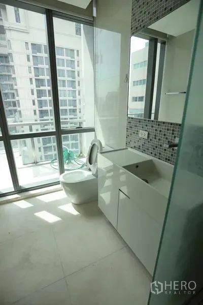 Condominium for rent or sale in Watthana, Bangkok - Modern bathroom with floor-to-ceiling windows, mosaic tile accent, vanity cabinet, and glass shower.