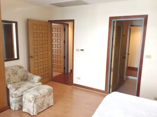 คอนโด ให้เช่าในPathum Wan, Bangkok - มุมห้องนอนพร้อมเก้าอี้ลายดอกไม้ ประตูไม้ และทางเข้าสู่ห้องน้ำในตัว