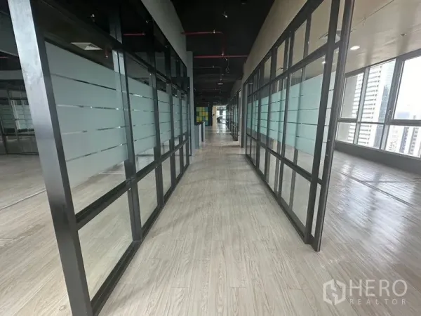 办公空间 出租在Bang Rak, Bangkok - 长走廊，两侧玻璃隔墙与木纹地面，临窗采光