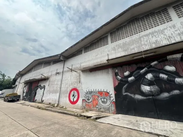 货栈 出租在Khlong Toei, Bangkok - 仓库外立面，宽卷闸与装卸口，墙面街头涂鸦