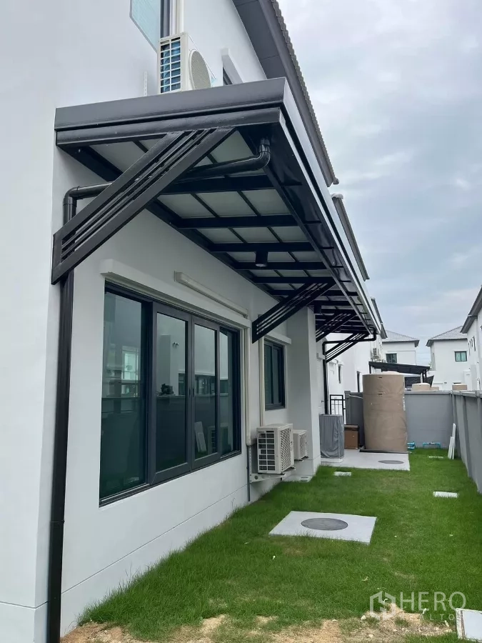 Detached House for rent or sale in Bang Phli, Samut Prakan - Side yard with green lawn, metal awnings, and outdoor air-conditioning units along the wall.