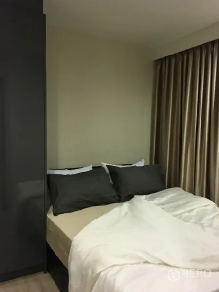 Condominium for sale in Pathum Wan, Bangkok - Cozy bedroom with double bed, dark pillows, floor-to-ceiling blackout curtains, and a sleek wardrobe.