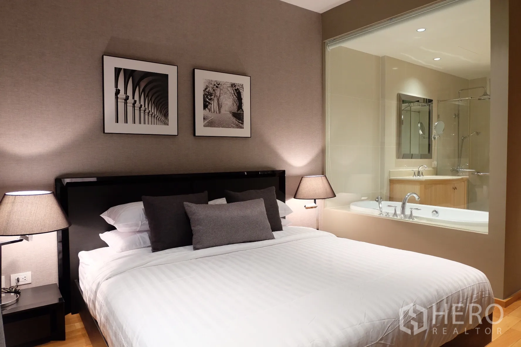 Condominium for rent in Sathon, Bangkok - Master bedroom with king bed, bedside lamps, framed art and a glass window to the ensuite bathroom with bathtub.