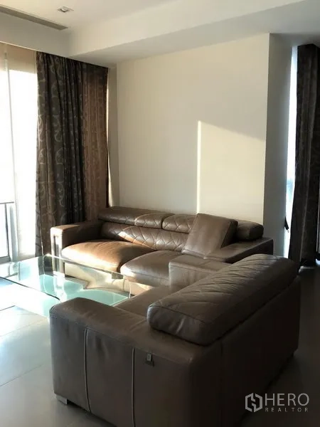 คอนโด ให้เช่าหรือขายในKhlong San, Bangkok - ห้องนั่งเล่นสว่าง โซฟาหนังสีน้ำตาล โต๊ะกระจก และผ้าม่านสูงจรดเพดาน