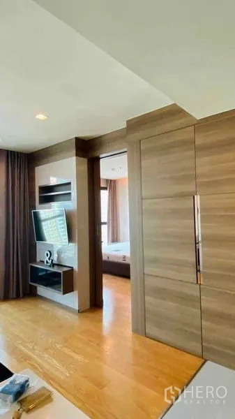 Condominium for rent or sale in Bang Rak, Bangkok - Hallway with built-in wooden wardrobes and wall-mounted TV unit leading toward the bedroom.
