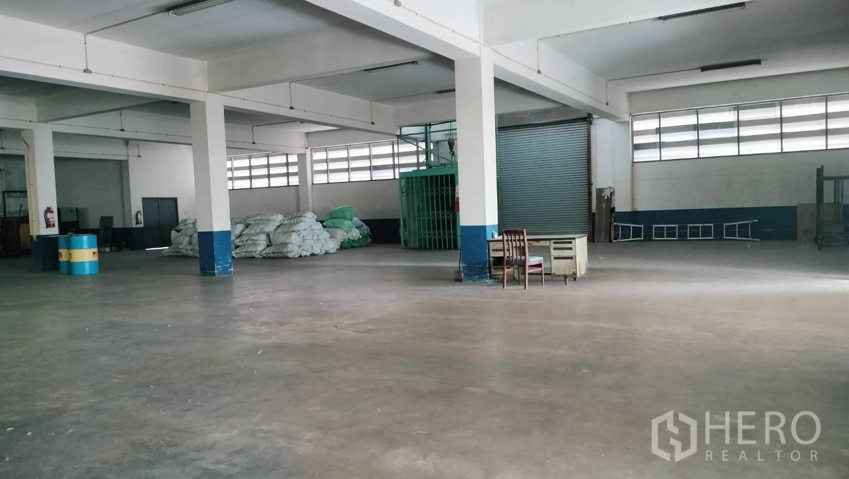 Factory for rent in Lat Krabang, Bangkok - Spacious production hall with concrete floor, columns, roller shutter door, and a small desk.