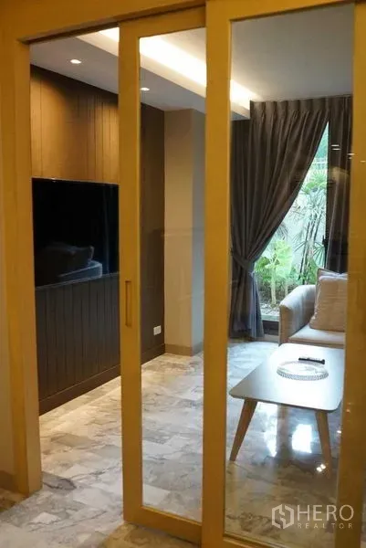 公寓 出租在Watthana, Bangkok - 木框推拉玻璃门通向带沙发的休闲室，可见花园景。