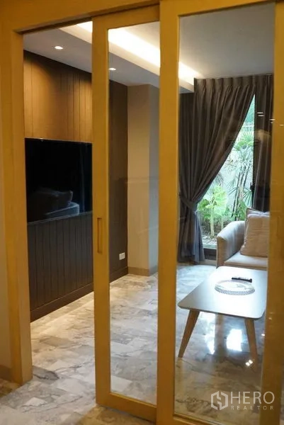 公寓 出租在Watthana, Bangkok - 木框推拉玻璃门通向带沙发的休闲室，可见花园景。