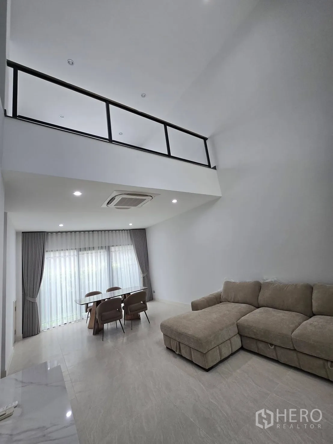 Semi-detached House for rent in Suan Luang, Bangkok - Double-height living room with mezzanine railing above and sectional sofa below.