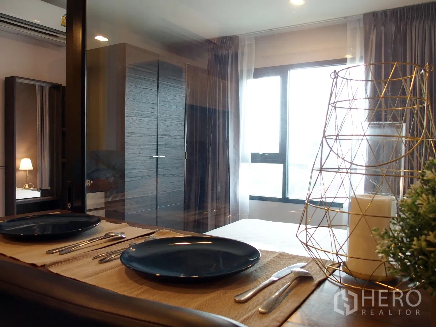 Condominium for rent in Huai Khwang, Bangkok - Dining nook in a Bangkok condo beside a window and glass partition overlooking the bedroom with wardrobe and sheer curtains.