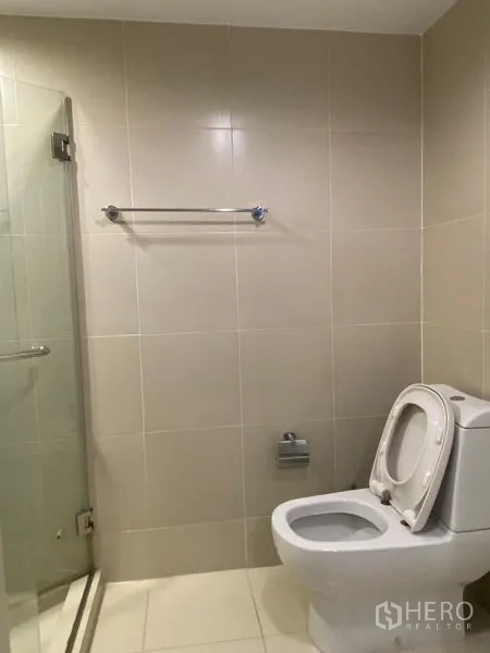 Condominium for rent - Toilet area with glass shower enclosure and towel rail on tiled walls.