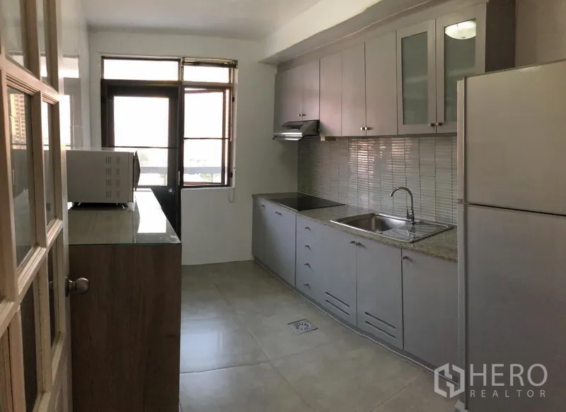 公寓 出租在Watthana, Bangkok - 封闭式厨房，长台面与灰色橱柜，马赛克墙面，水槽、炉灶、油烟机、冰箱和微波炉。