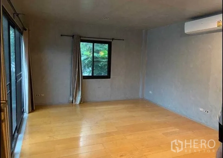 Detached House for rent or sale in Wang Thonglang, Bangkok - Spacious bedroom with wooden flooring, window, air conditioner and sliding glass door.