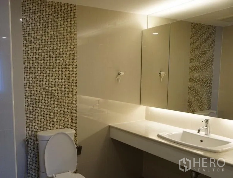 Condominium for rent in Watthana, Bangkok - Modern bathroom vanity with large mirror and mosaic accent wall.