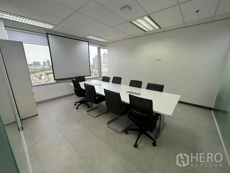 Office Space for rent - Conference room with long white table, black chairs, projector screen and city skyline view.