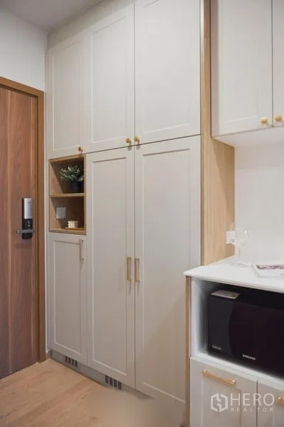 Condominium for sale in Suan Luang, Bangkok - Entryway storage with tall kitchen cabinets, gold pulls and a built-in microwave.