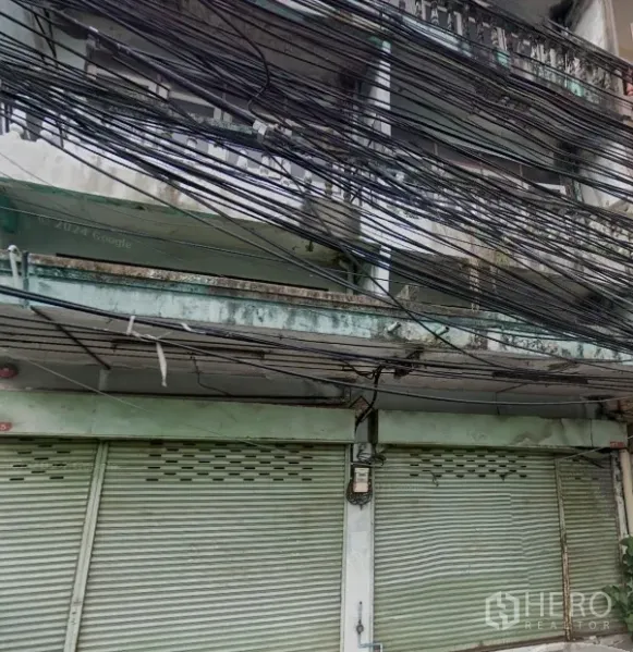 店屋 出租在Phra Khanong, Bangkok - 老式商铺外立面，金属卷闸门、阳台与密集电缆。