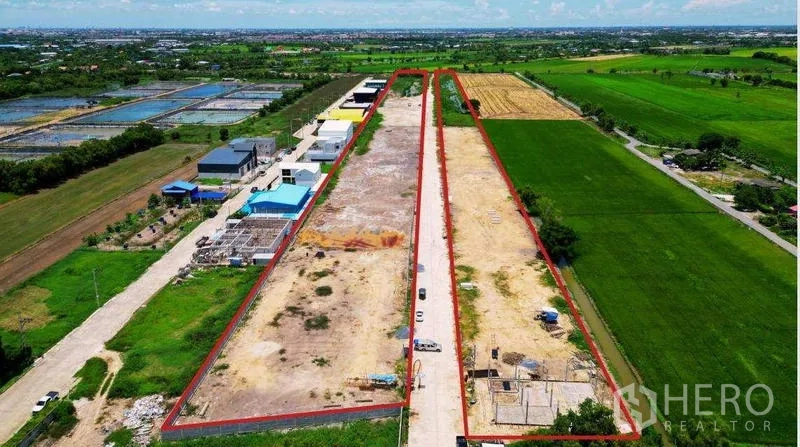 Land for sale in Bang Bua Thong, Nonthaburi - Aerial view of a long rectangular land plot outlined in red with a central concrete road, adjacent warehouses, and green fields in Bang Bua Thong.